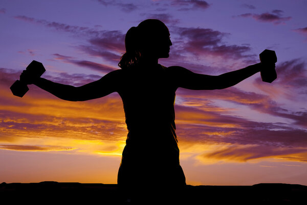 Silhouette of a woman doing lateral raises with weights.