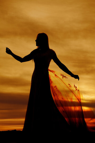 A silhouette of a woman in her wedding dress holding on to her train in the sunset.