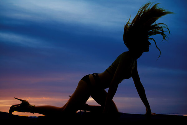 A silhouette of a woman in bikini flipping her hair on the ground.