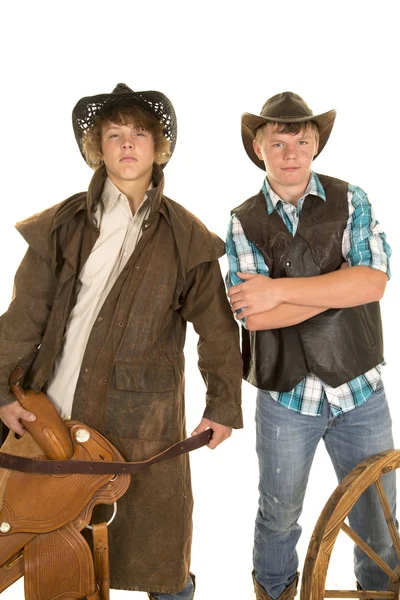 Two young cowboys with saddle and wagon wheel — Stock Photo, Image