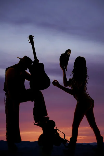 Silhouette cowgirl shorts butt out hold hat cowboy with guitar — Stock Photo, Image