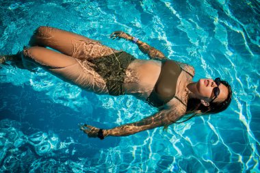 Lüks tatil köylerinde havuzda poz veren şık güneş gözlüklü zarif kızın moda portresi. Neşeli artı boyut genç kız eğleniyor. Mutlu, pozitif duygu, yaz tarzı..