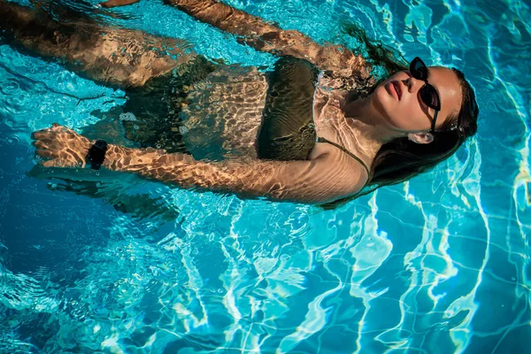 Fashion portrait of graceful cute girl in stylish sunglasses posing in the pool during holidays on luxury resort. Cheerful plus size teenage girl enjoying. happy, positive emotion, summer style.