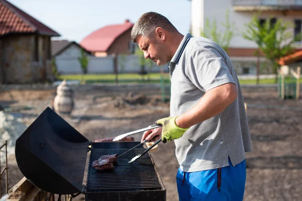 Close-up portrait of a cheerful man grilling meat on barbecue outdoors.