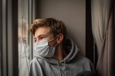 Evde, karantinada koruyucu maskesiyle üzgün görünen genç çocuk Covid-19 Coronavirus salgını sırasında okulu ve özgürlüğü kaçırıyor.