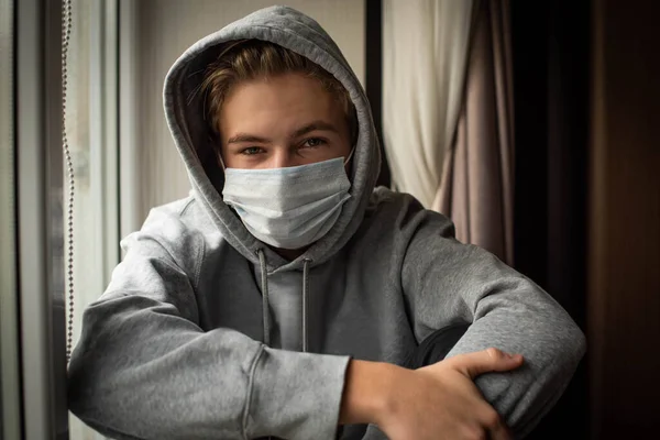 悲しい10代の男の子は自宅でコロナウイルス危機によって閉じ込められ 家を出ることができずに窓の外に退屈しているように見えます 集中した背景 — ストック写真