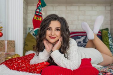 Mutlu genç bir kadın Noel ağacının yanında oturuyor. Noel ağacının yanındaki şöminenin yanında kıvırcık saçlı mutlu genç bayan hediyeleri. Yeni yıl konsepti. Xmas.