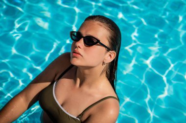 Lüks tatil köylerinde havuzda poz veren şık güneş gözlüklü zarif kızın moda portresi. Neşeli artı boyut genç kız eğleniyor. Mutlu, pozitif duygu, yaz tarzı..