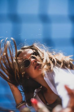 Güzel, genç ve büyük beden bir model. Hipster tarzı beyaz, şık kıyafetler giyiyor. Tenis kortunda güneş gözlüğü takan moda bir kız. Orijinal gölge.