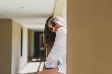 Yazın hippi tarzı beyaz şık kıyafetler giyen güzel, gülümseyen kiracı modelinin portresi. Moda kızı arka planda poz veriyor. Güneş gözlüklü komik ve pozitif kadın