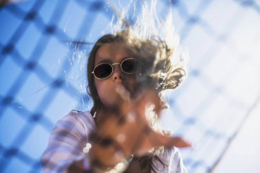 Güzel, genç ve büyük beden bir model. Hipster tarzı beyaz, şık kıyafetler giyiyor. Tenis kortunda güneş gözlüğü takan moda bir kız. Orijinal gölge.