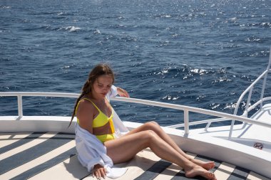 Neşeli genç kadın portresi. Yelkenli yatın güvertesinde oturan mutlu genç kız, yaz gezisinde tropikal denizde adaları keşfederken eğleniyor. Seyahat macerası, yat gezisi.