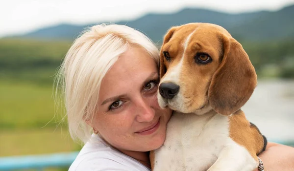 Cute woman close up portrait, hugging beagle dog at the walk. Smiling young woman enjoying good day and posing with pet. Real people concept.