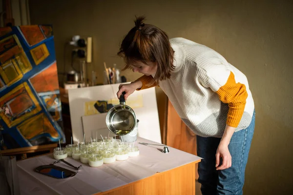 女人把融化的蜡倒入琥珀蜡烛容器 生态和素食行业 大豆蜡蜡烛配件 用爱心手工做的远程工作 网上商店 工作场所 — 图库照片