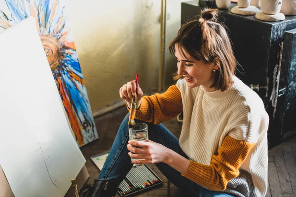 Beautiful woman painting. Girl in Painting Studio. Talented Female Artist Working on a Modern Abstract Oil Painting, Gesturing with Broad Strokes Using Paint Brush. Dark Creative Studio