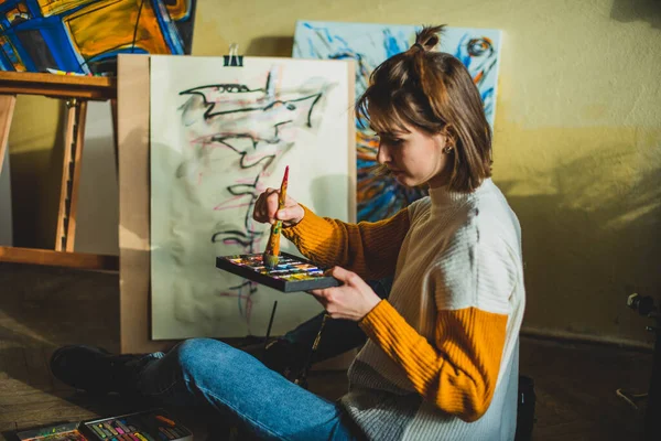 Beautiful woman painting. Girl in Painting Studio. Talented Female Artist Working on a Modern Abstract Oil Painting, Gesturing with Broad Strokes Using Paint Brush. Dark Creative Studio