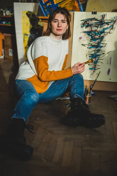 Beautiful woman painting. Girl in Painting Studio. Talented Female Artist Working on a Modern Abstract Oil Painting, Gesturing with Broad Strokes Using Paint Brush. Dark Creative Studio