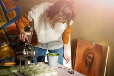Erimiş balmumunu kehribar mumların içine döken kadın. Ekolojik ve vejetaryen işleri. Soya mumu aksesuarları. Sevgiyle el yapımı. Uzak çalışma, çevrimiçi dükkan, işyeri