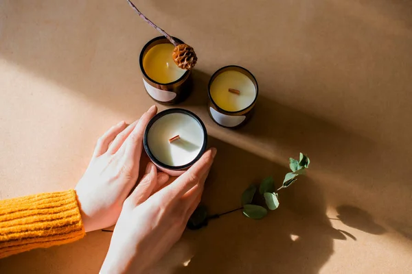 wick candles. Handmade candle from paraffin and soy wax in glass with leaf on craft background. Let flay. Candle making. Top view. Womans hands holding the candles