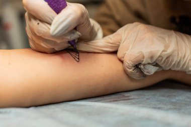 Ana dövme müşterilerin dövmelerindeki kırmızı boyayı çizer. Siyah steril eldivenli pembe dövme makinesi tutan dövme sanatçısı profesyonel mavi paspas üzerinde çalışıyor..