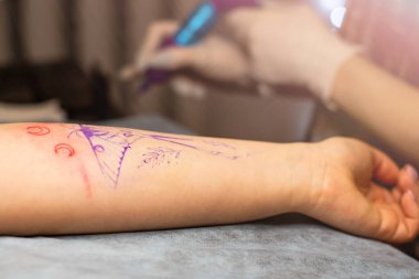 Ana dövme müşterilerin dövmelerindeki kırmızı boyayı çizer. Siyah steril eldivenli pembe dövme makinesi tutan dövme sanatçısı profesyonel mavi paspas üzerinde çalışıyor..