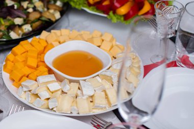 Bardaklar beyaz masada. Masada meyve, tabak ve yemek servisi yapan bir oda. Peynir, bal, salata, atıştırmalık.