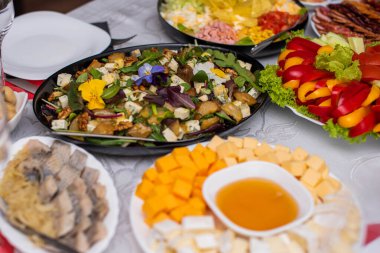 Bardaklar beyaz masada. Masada meyve, tabak ve yemek servisi yapan bir oda. Peynir, bal, salata, atıştırmalık.