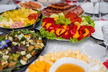 Bardaklar beyaz masada. Masada meyve, tabak ve yemek servisi yapan bir oda. Peynir, bal, salata, atıştırmalık.