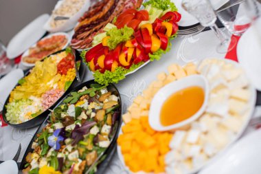 Bardaklar beyaz masada. Masada meyve, tabak ve yemek servisi yapan bir oda. Peynir, bal, salata, atıştırmalık.