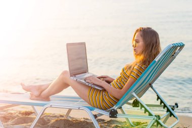 Kumsalda dizüstü bilgisayar kullanan genç bir kadın. Serbest çalışma kavramı