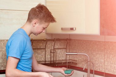 Çocuk lavaboda bulaşıkları yıkıyor.