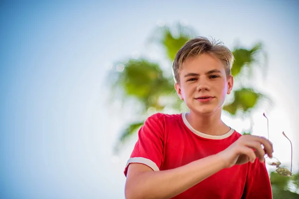Yakışıklı Genç Çocuk Sahilde Kırmızı Tişörtlü Palmiye Ağaçlarının Altında Poz — Stok fotoğraf