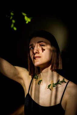 Yüzünde ve vücudunda çizgiler şeklinde gölge desenleri olan güzel bir genç kızın portresi. Moda, güzellik. Yeşil yapraklı kadın köprücük kemiği, alçı..