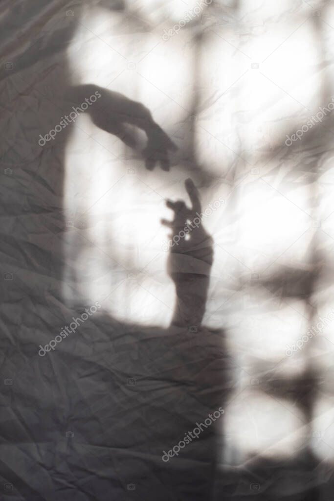 Grey shadows of hands reaching each other on the wall. Abstract blurred effect. Focus on shadows.