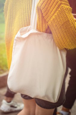 Boş beyaz çanta bez kumaş ve kabzası da tasarım. Çevreci kadınların el ele tutuşması ya da yeşil yapraklar üzerinde tekrar kullanılabilen alışveriş torbaları. Plastik poşet ve ekoloji konsepti yok. Boşluğu kopyala.