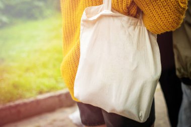 Boş beyaz çanta bez kumaş ve kabzası da tasarım. Çevreci kadınların el ele tutuşması ya da yeşil yapraklar üzerinde tekrar kullanılabilen alışveriş torbaları. Plastik poşet ve ekoloji konsepti yok. Boşluğu kopyala.