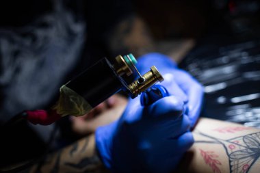 Kuaförde dövmenin kesilip atılmış hali. Profesyonel bir dövme sanatçısı dövme makinesinin iğnesini kullanarak cilde mürekkep yerleştirir. Stüdyoda çalışan profesyonel bir dövmeci..