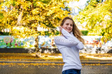 Sonbaharda dışarıda yürüyen güzel, tatlı bir genç kız. Gülümseyen genç bayan, sonbahar havasının tadını çıkarıyor..