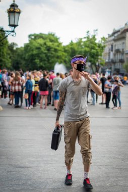 Sokak tarzı giyinmiş, boynu zincirli, mor bandana ve siyah tıbbi maskeli olumlu bir adam. Gençlik ve yaşam tarzı konsepti. Kirli şehir havası.