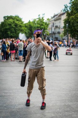 Sokak tarzı giyinmiş, boynu zincirli, mor bandana ve siyah tıbbi maskeli olumlu bir adam. Gençlik ve yaşam tarzı konsepti. Kirli şehir havası.