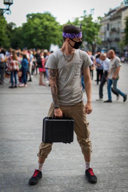 Sokak tarzı giyinmiş, boynu zincirli, mor bandana ve siyah tıbbi maskeli olumlu bir adam. Gençlik ve yaşam tarzı konsepti. Kirli şehir havası.