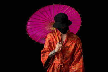 Sokak tarzı giyinmiş, boynu zincirli kırmızı kimonolu, siyah panama ve siyah tıbbi maskeli bir adam. Gençlik ve yaşam tarzı konsepti. Siyah üzerine izole edilmiş..