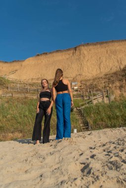 Kumsalda koşan ve yaz tatilinin tadını çıkaran mutlu gençler. Sahilde yürüyen iki güzel kız.