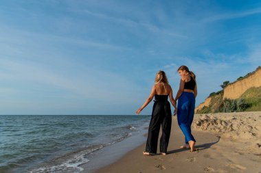 Kumsalda koşan ve yaz tatilinin tadını çıkaran mutlu gençler. Sahilde yürüyen iki güzel kız.