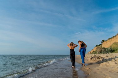 Kumsalda koşan ve yaz tatilinin tadını çıkaran mutlu gençler. Sahilde yürüyen iki güzel kız.