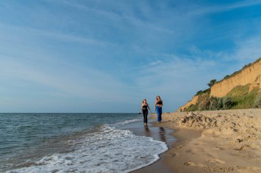 Kumsalda koşan ve yaz tatilinin tadını çıkaran mutlu gençler. Sahilde yürüyen iki güzel kız.