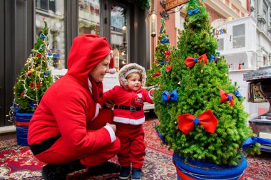 Noel aile tatili konsepti. Mutlu Noeller ve mutlu tatiller. Anne ve kızı Noel Baba kostümü giymiş. Eğlenceli yürüyüşler. Anne kızını kollarında tutuyor, samimi bir gülümseme..