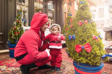Noel aile tatili konsepti. Mutlu Noeller ve mutlu tatiller. Anne ve kızı Noel Baba kostümü giymiş. Eğlenceli yürüyüşler. Anne kızını kollarında tutuyor, samimi bir gülümseme..