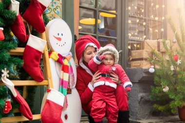 Noel aile tatili konsepti. Mutlu Noeller ve mutlu tatiller. Anne ve kızı Noel Baba kostümü giymiş. Eğlenceli yürüyüşler. Anne kızını kollarında tutuyor, samimi bir gülümseme..