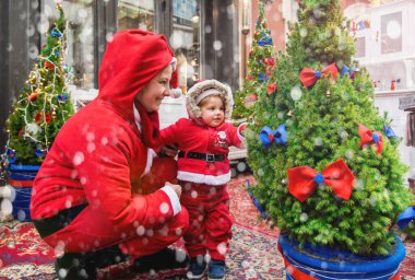Noel aile tatili konsepti. Mutlu Noeller ve mutlu tatiller. Anne ve kızı Noel Baba kostümü giymiş. Eğlenceli yürüyüşler. Anne kızını kollarında tutuyor, samimi bir gülümseme..